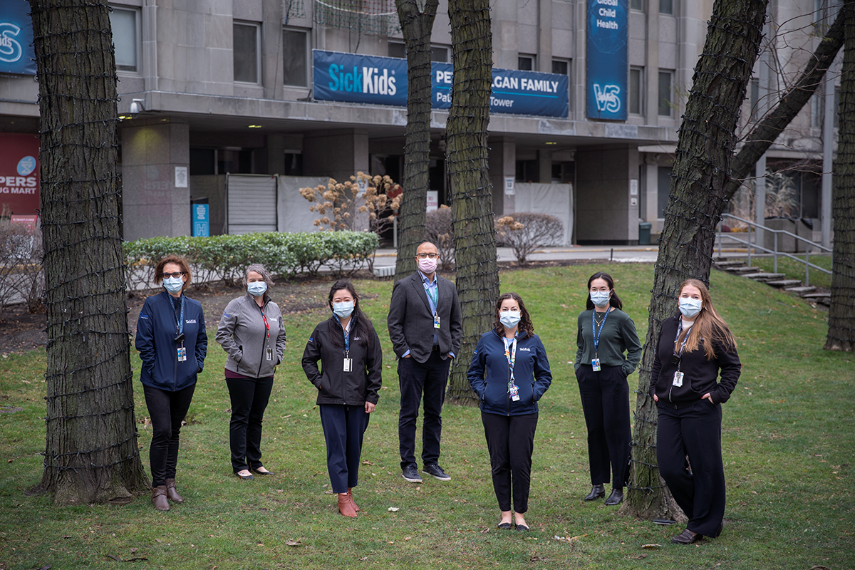 A group of people in masks, standing outside by the hospital entrance.