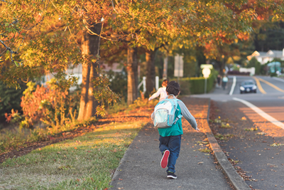 A young boy running home from school next to a road.