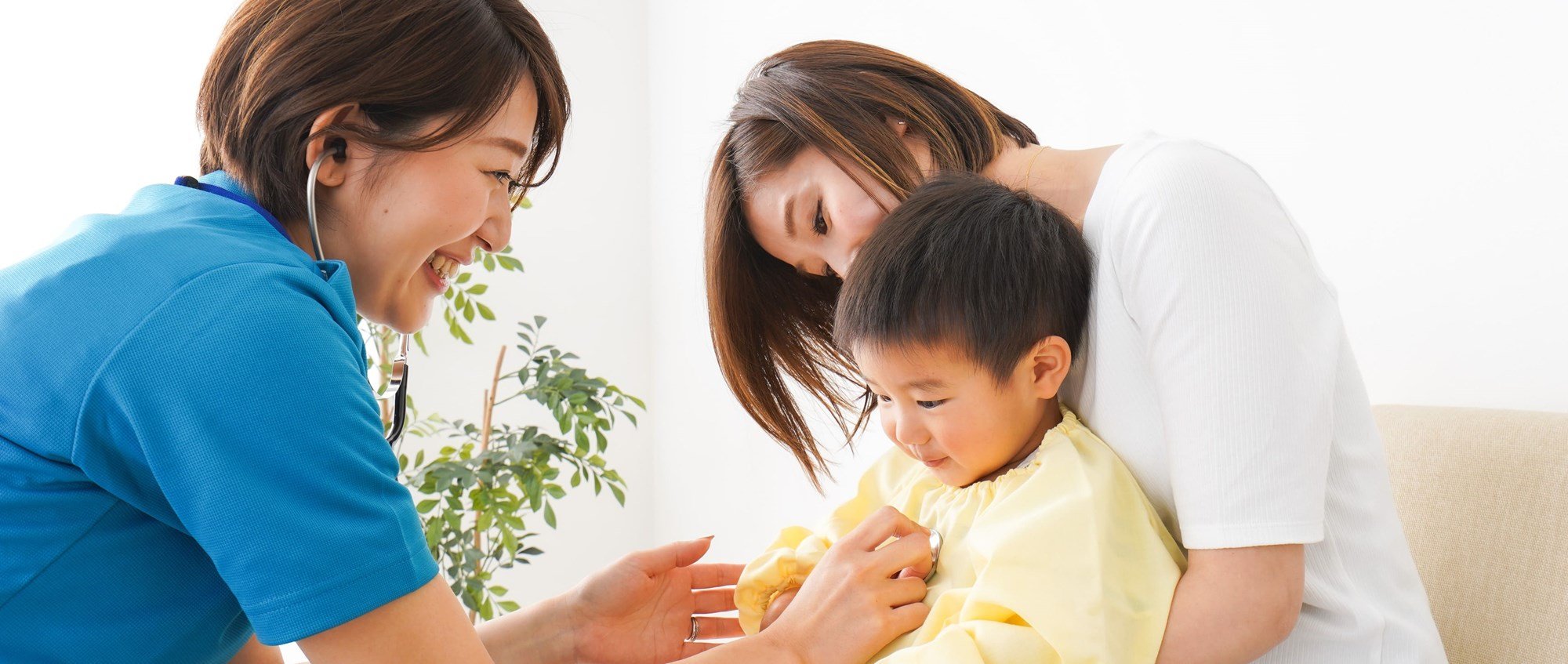 doctor taking heartbeat of young patient smiling in his mom's lap