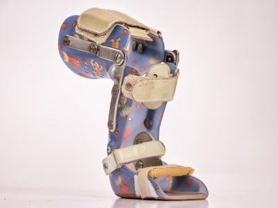 A child-size knee orthosis with metal joints along the side and straps to secure the orthosis in place.