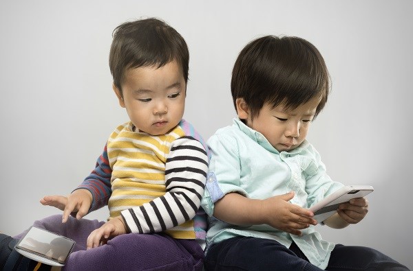 Two babies sit back to back, each holds a mobile device.