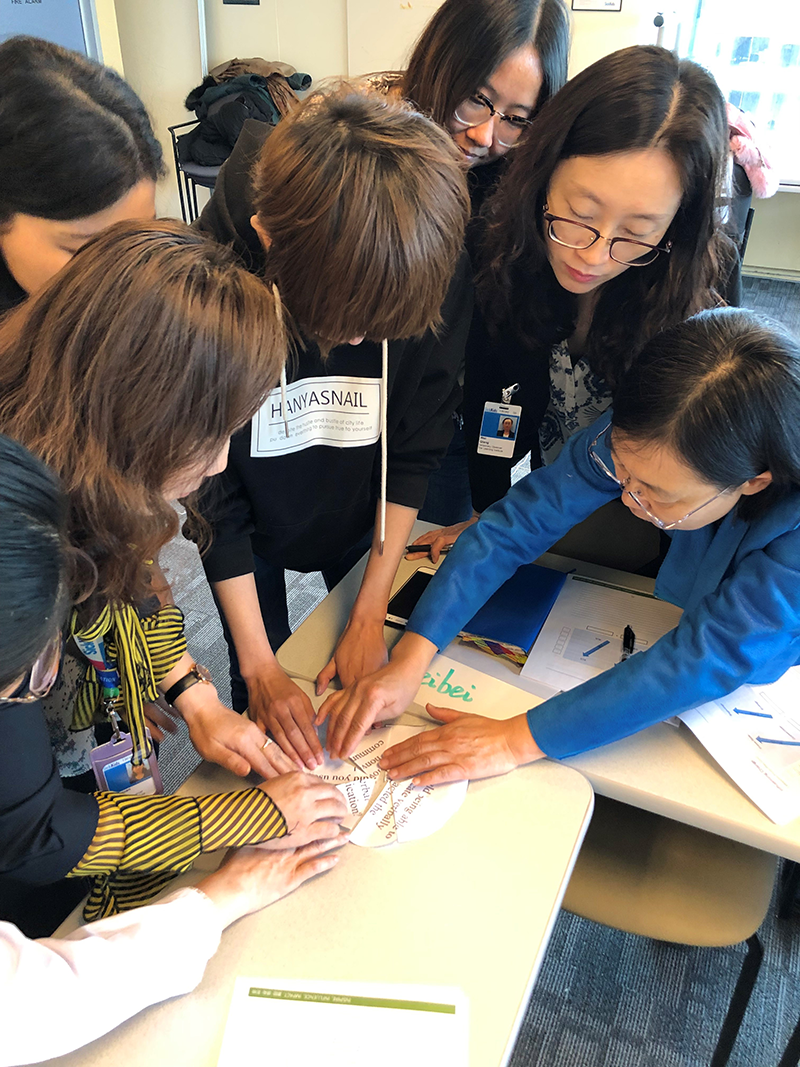 A group of staff standing around a desk, working together to assemble and hold a paper puzzle