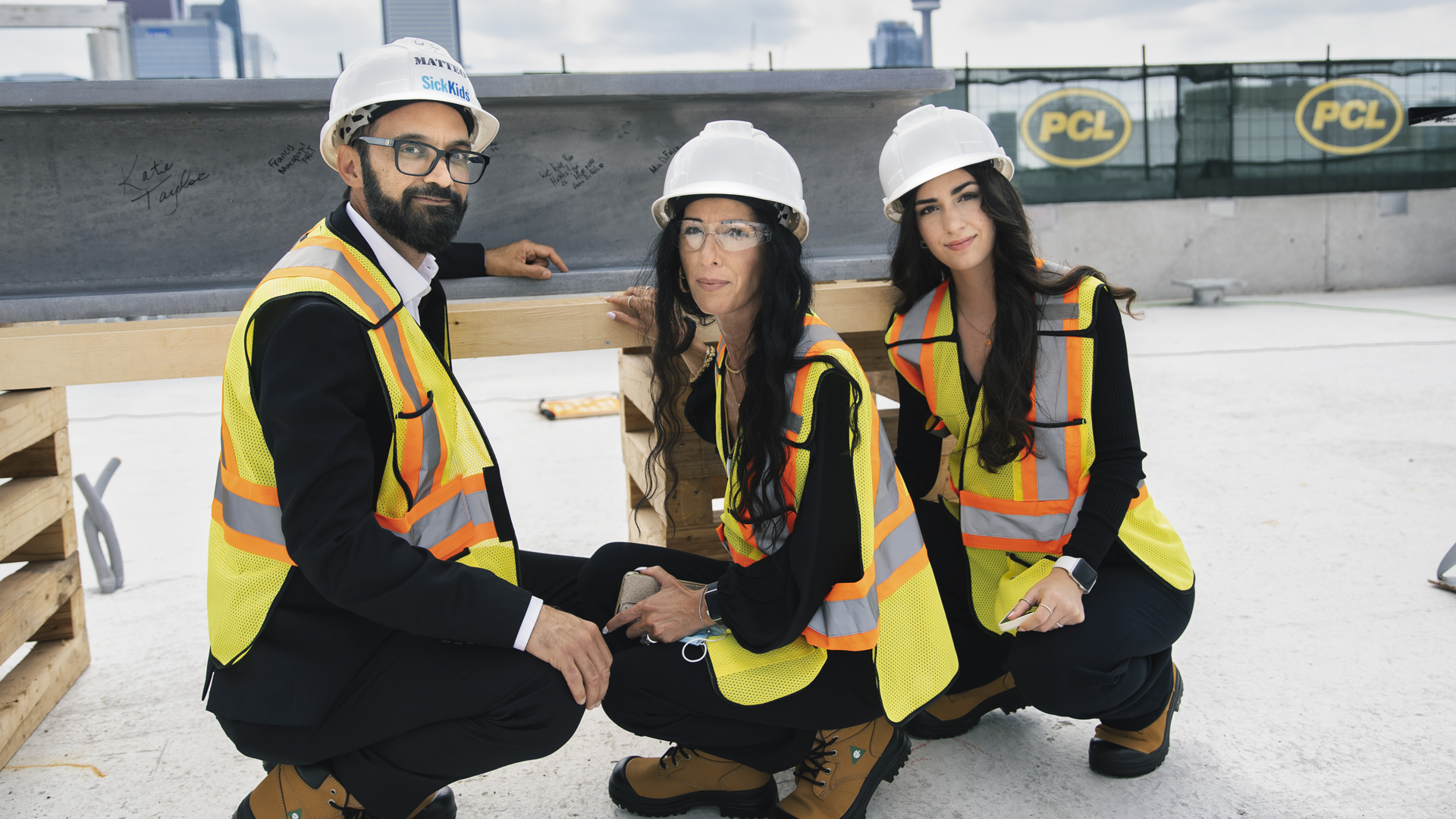 A man, woman and teenage girl wearing construction gear crouch down in front of a large steel beam covered in signatures