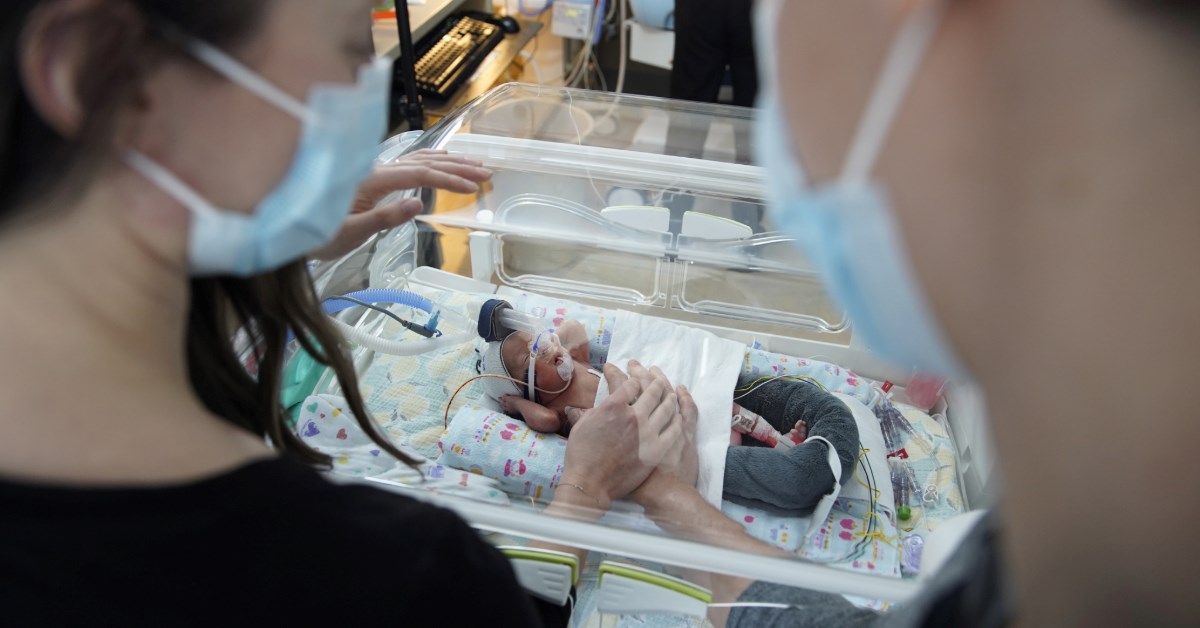 An over the shoulder view of Erica and Brett Morrison looking at their son Jeffrey, lying in his incubator in the SickKids NICU