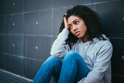 Teen sits leaning against a wall with head in her hand.