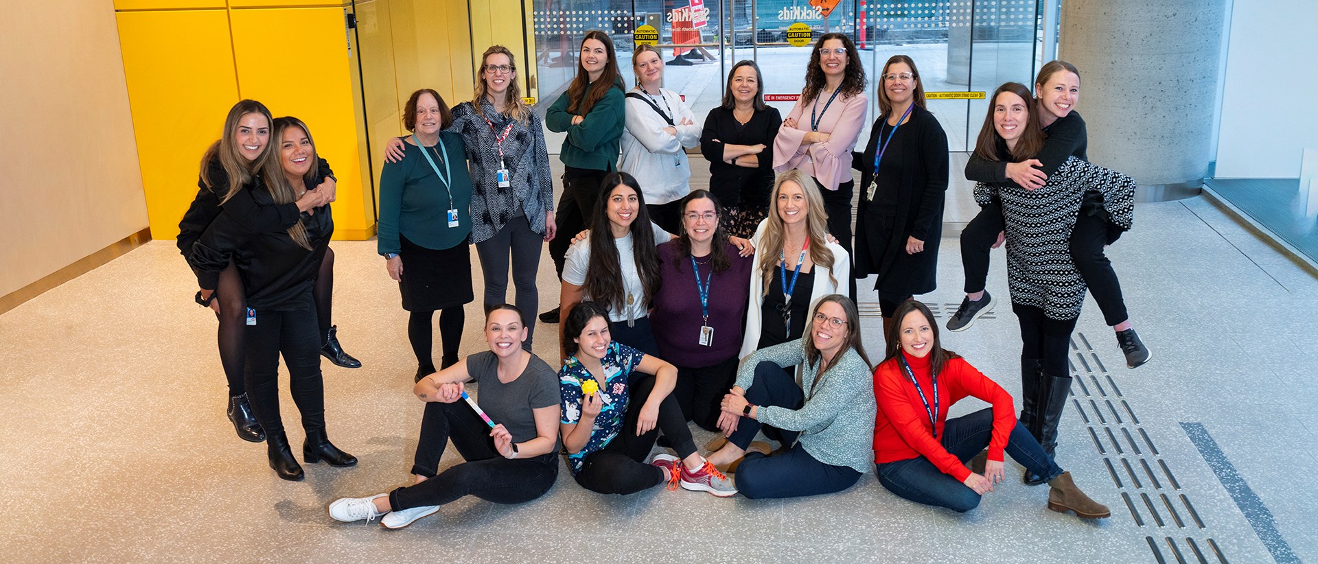 A group of 18 people smiling and posing together for a photo on the main floor of the Patient Support Centre. 