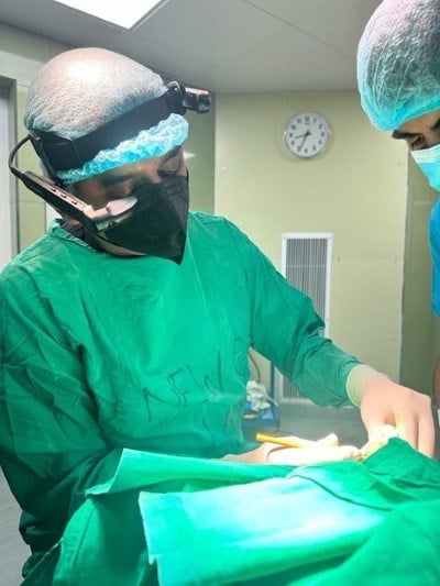 A person in surgical gear, wearing a smart glasses headset while performing an operation.