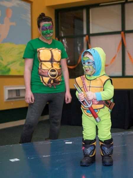 Little boy dressed as a turtle with face makeup on. A woman dressed similarly stands behind him.