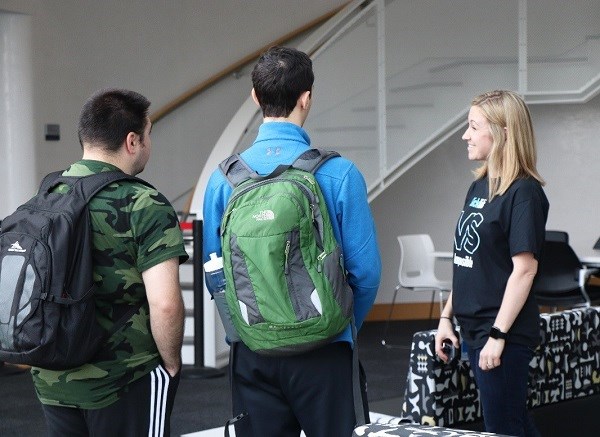 Staff member in SickKids shirt talks to two visitors wearing backpacks.