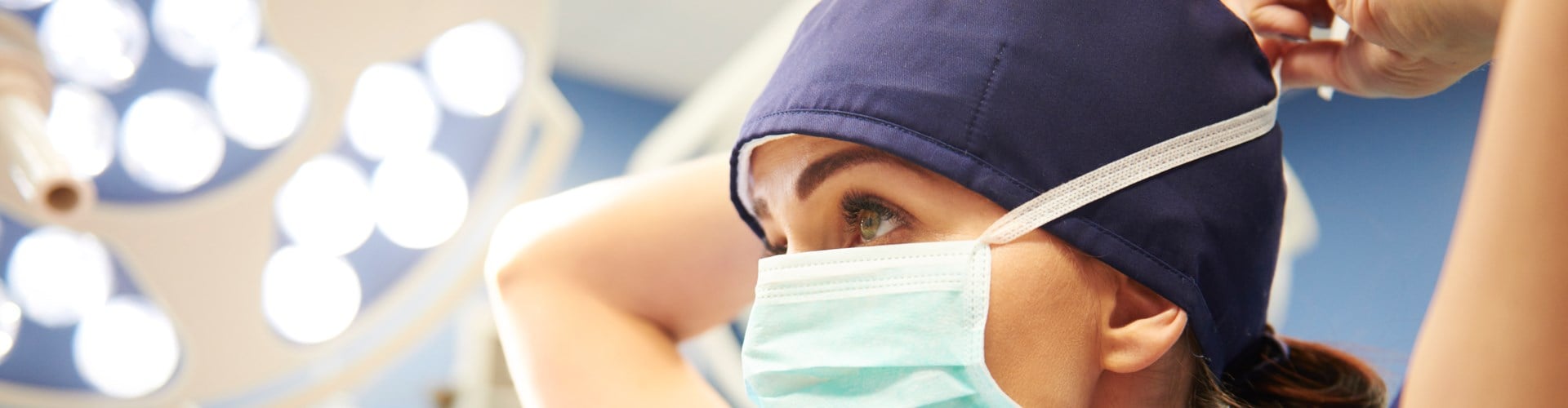 Woman in medical scrubs tying PPE mask around her head