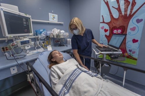 A health-care professional assisting a patient who is lying in a bed.