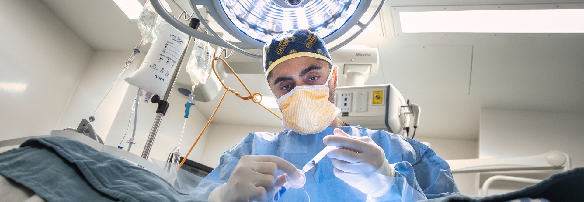 Surgeon in full PPE loading a syringe in an operating room with a bright light above