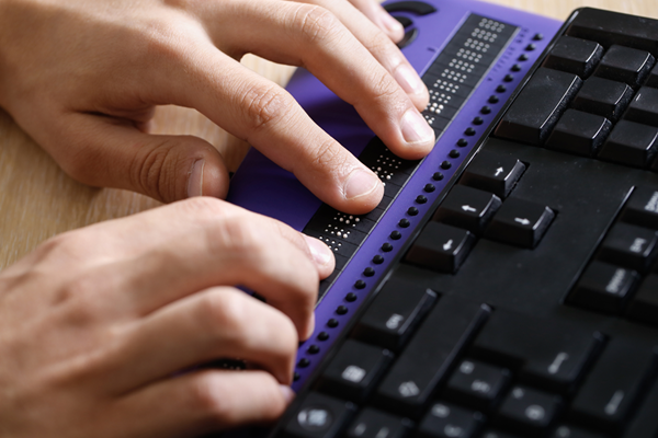Person's hands using computer with braille computer keyboard