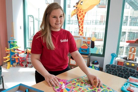 A volunteer in a SickKids t-shirt in a room with colourful toys.