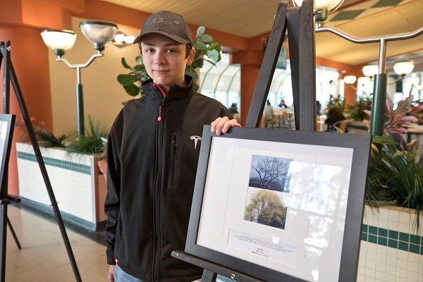 Teen stands next to framed photograph of trees.