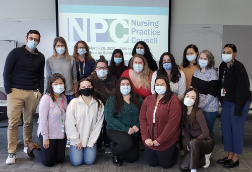 A group of Nursing Practice Leaders wearing surgical masks gather in front of a projector with a logo that reads, “Nursing Practice Council.”