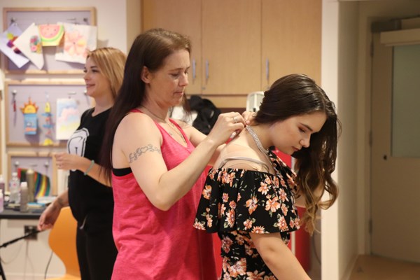 A woman fastens a necklace around a girl's neck.