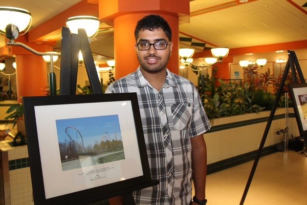 Teen stands next to framed photo of a rollercoaster.