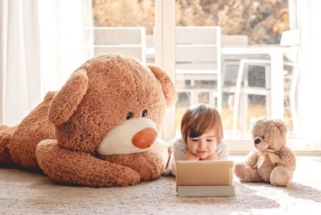 Toddler engaging with a learning ipad beside two big teddy bears