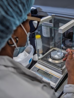 A person in a lab coat and cap measuring nutrients on a weighing scale.