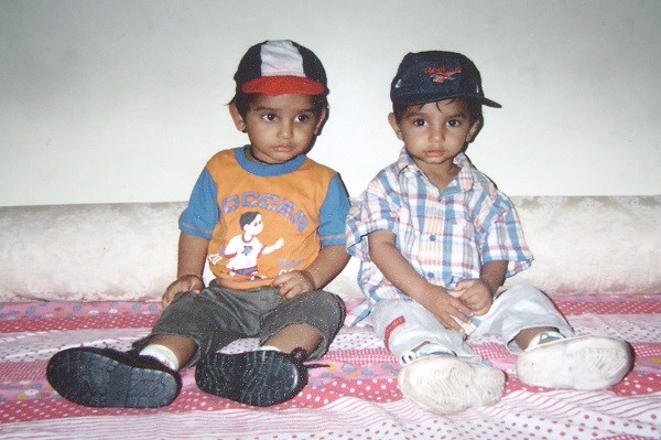 Two very young boys seated side by side, they are wearing clothes that appear from the late 1980s or early 1990s.