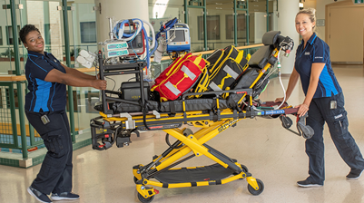 Two people push a medical stretcher loaded with equipment.