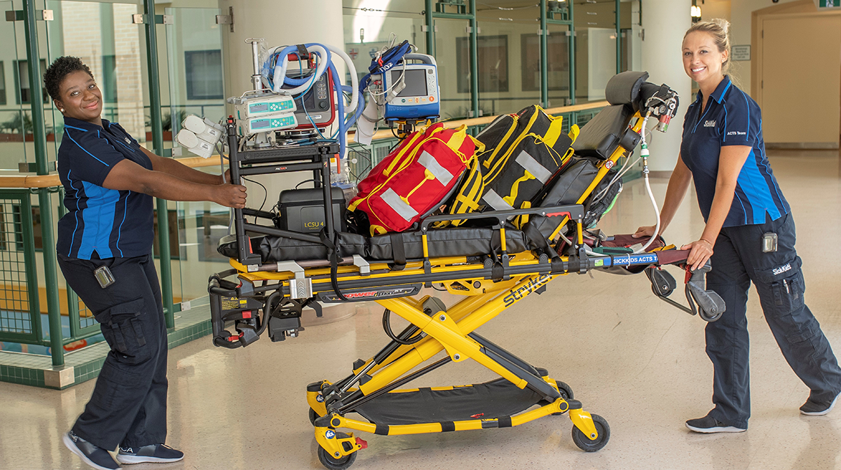 Two people push a medical stretcher loaded with equipment.