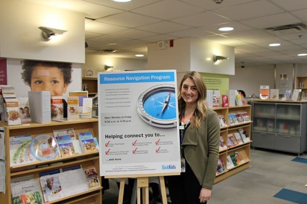 Woman stands next to bulletin board inside a library.