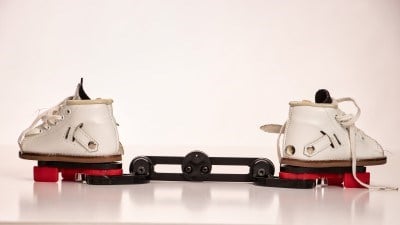 White leather lace-up baby boots attached to a red and black bar are displayed in front of a white background.