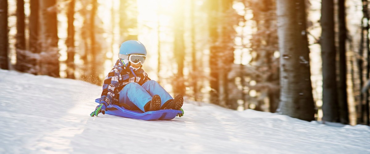 Child sitting on a sled wearing a helmet and ski goggles