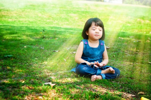 Young child in blue denim sitting cross-legged on grass, meditating peacefully in sunshine.RetryClaude can make mistakes. Please double-check responses.