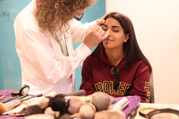A makeup artist applies eyeshadow to a young woman.