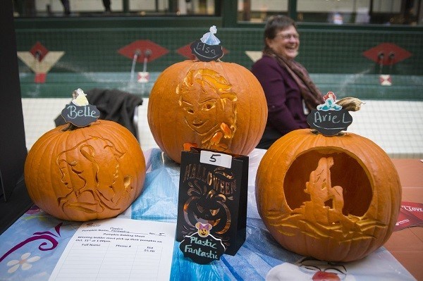 Three pumpkins each carved with the face of a different Disney princess: Belle, Elsa and Ariel.
