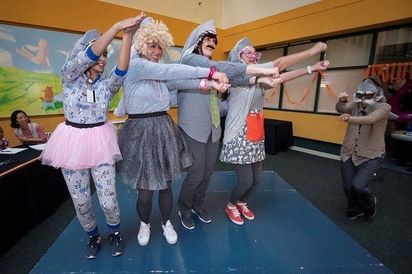 Group of adults dressed as sharks dance with their arms raised.