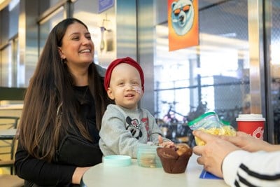 A child with a feeding tube attached seated on their parent's lab at a table