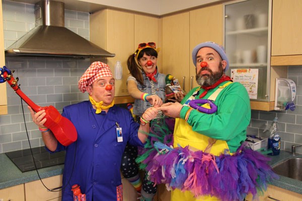 Three clowns pose together making funny faces.