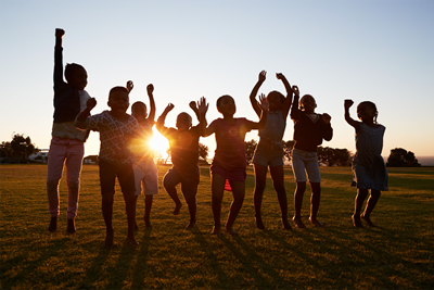 Eight children cheering. The photo is taken as the children are mid-jump with their arms in the air with the setting sun in the background.