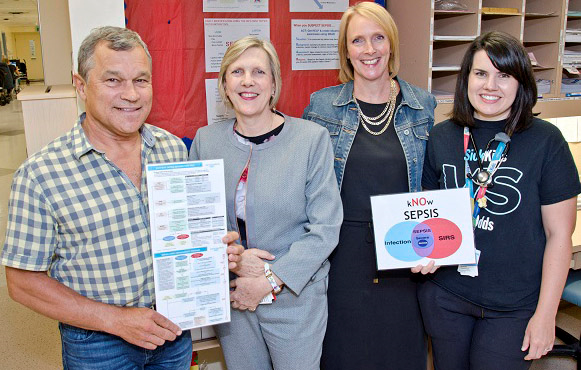 Team of four staff stand together showing two documents.