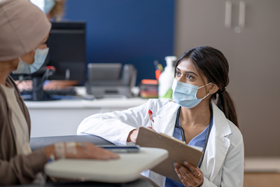 A doctor kneels in front of a young cancer patient holding a clipboard.