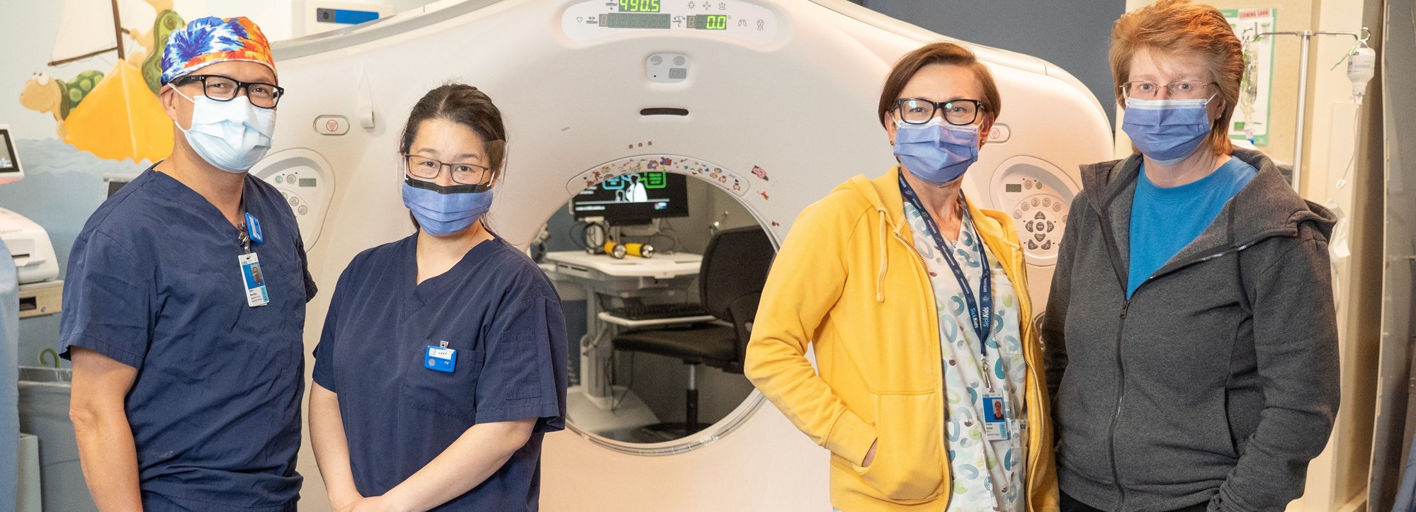 4 members of the atrium CT team in front of a CT scanner with PPE masks on and hospital scrubs