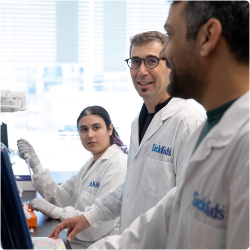 Adam Shlien and team members in SickKids branded lab coats standing at a lab bench and conversing.