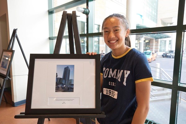 Young girl stands next to her photo, framed and on an easel.