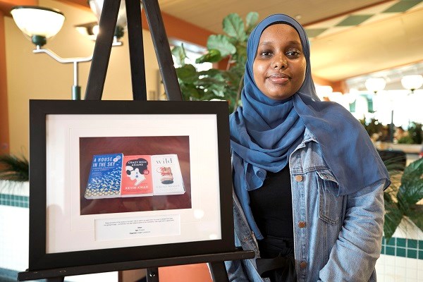 Young woman stands next to image of books, framed on an easel.