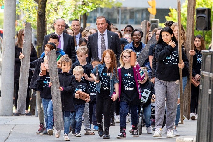 Peter Gilgan, Ronald Cohn and SickKids patients walk together on a street