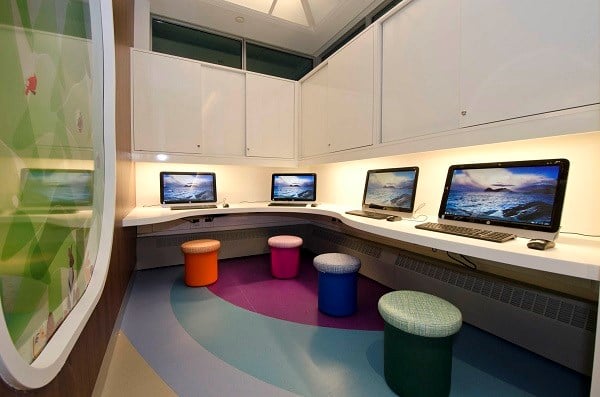 Four computers laid out on a corner desk, each with a stool.