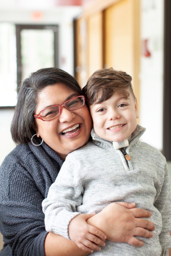 A parent and child smile, standing cheek to cheek.