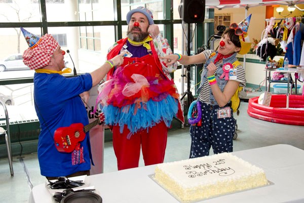 Three clowns stand together with a birthday cake in front of them.
