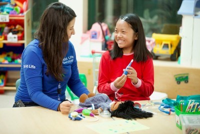 A person in a blue SickKids shirt that reads "Child Life Services" playing with a child.