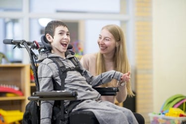 Smiling adolescent with assistive device and caregiver