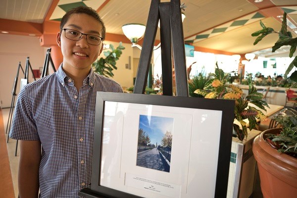 Teen boy stands next to framed image on an easel.